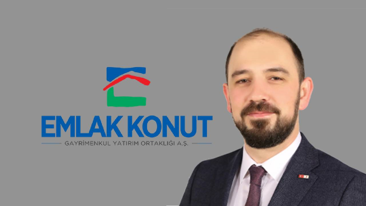 emlak konut genel müdürü yasir yılmaz, emlak konut logolu bir resmin önünde poz veriyor.