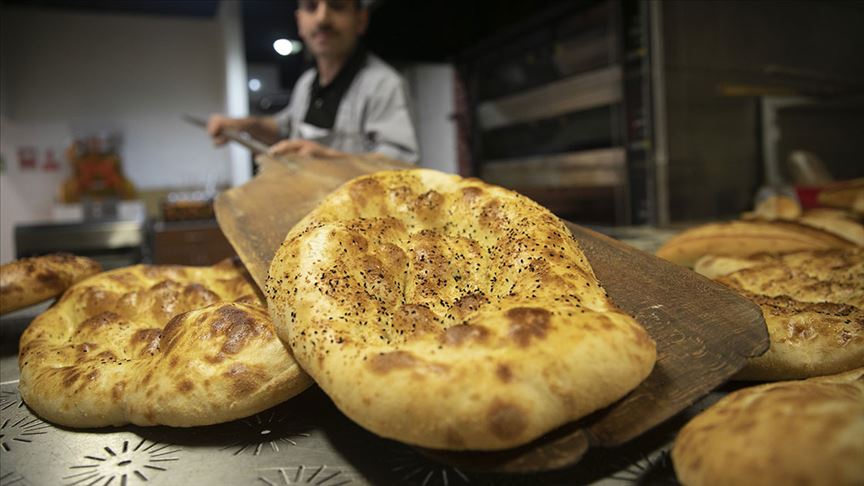 Ön planda susamlı ve altın sarısı renkli, 370 gramlık sıcak Ramazan pidesi, arka planda daha fazla pide sıralanıyor.