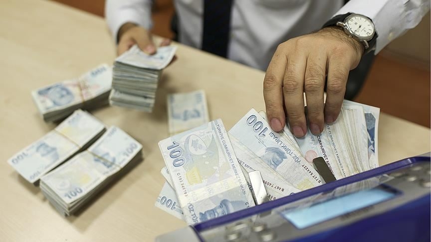 Bir banka çalışanı, para sayma makinesiyle Türk lirası banknotlarını sayarken görülüyor. Bu sahne, konut kredi faizleri düşecek mi sorusunu araştıranlar için finansal işlemleri ve kredi maliyetlerini çağrıştırıyor.