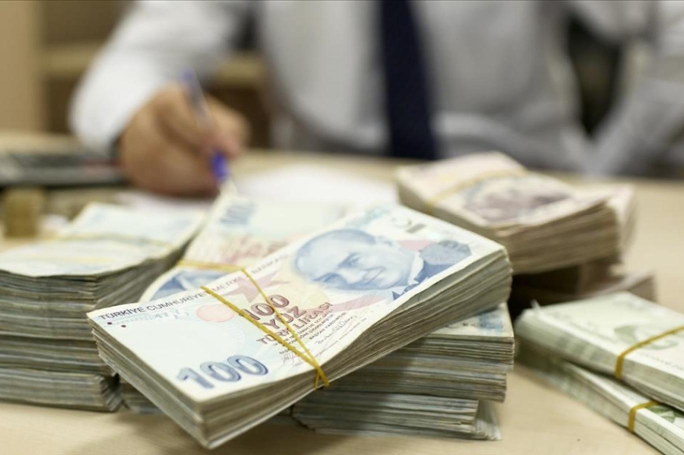 Bir banka çalışanı, masada yığılı Türk lirası banknotları üzerinde çalışırken görülüyor. Bu görüntü, konut kredi faizleri ve en uygun konut kredi faizi arayışındaki tüketiciler için finansal işlemleri temsil ediyor