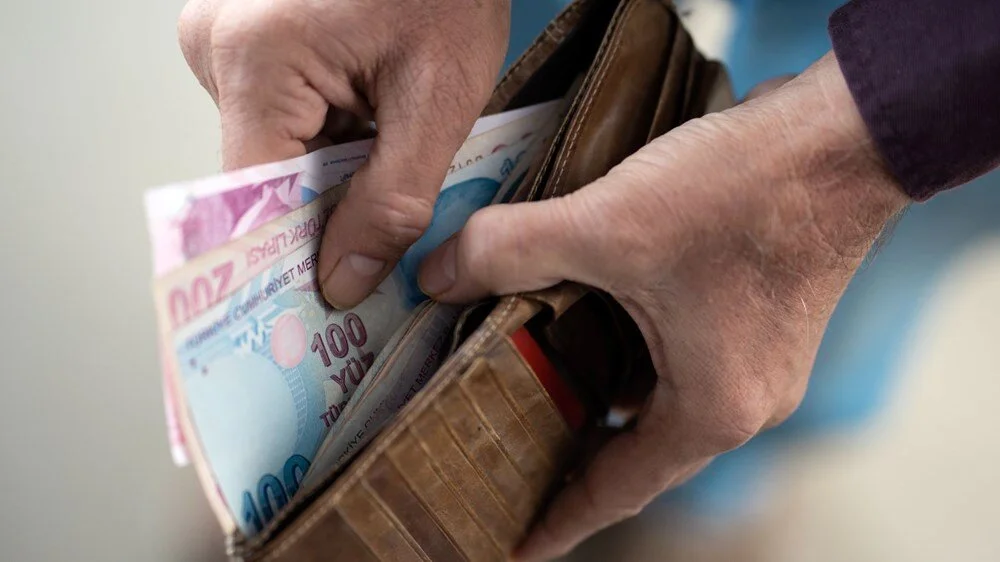 Mor kıyafetli bir emeklinin ellerinde 100 TL ve 200 TL banknotları tutarken çekilmiş fotoğrafı. Emekli banka promosyonu ödemelerini vurgulayan, yaşlı bireylerin finansal desteğini gösteren görüntü.